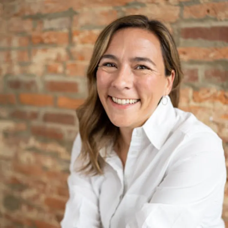 Person smiling, wearing a white shirt, with a brick wall background.