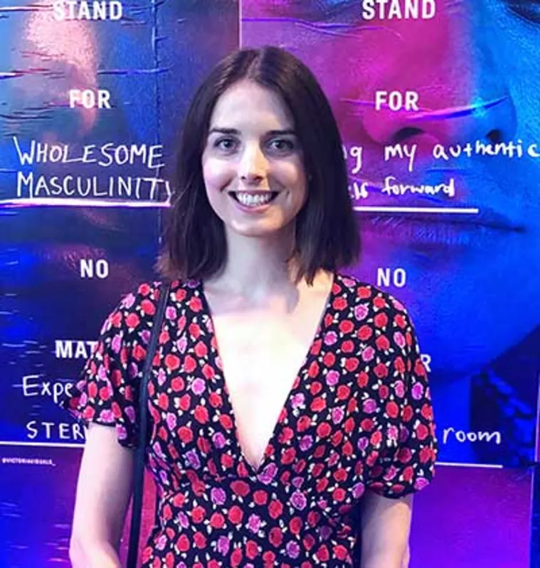Person smiling in front of a colorful background with text promoting positive masculinity. Wearing a floral patterned outfit.