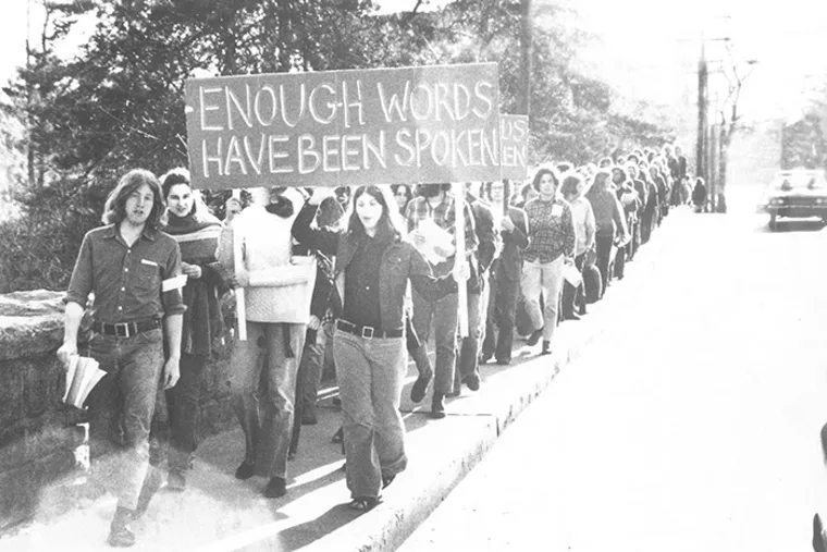 Protesters walk in a line holding a large sign reading "Enough words have been spoken" on a street.