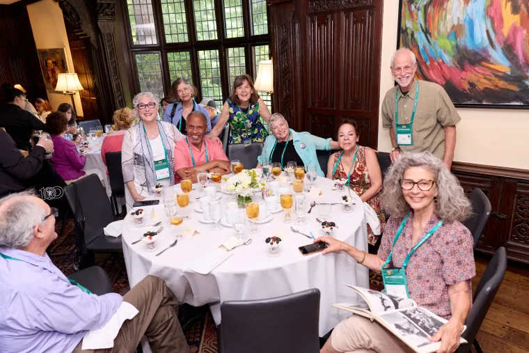 Group of people smiling around a table set with drinks and plates at a social event in a decorated room.