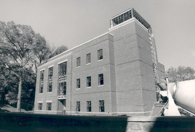 A brick building under construction with scaffolding and trees in the background, surrounded by construction equipment.