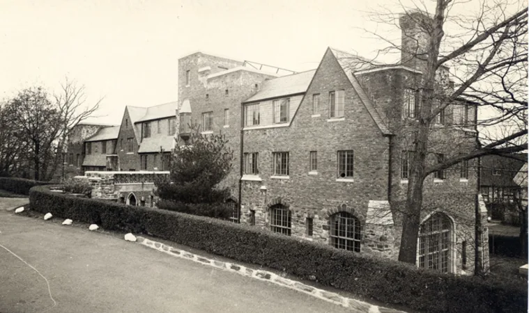 Historical brick building with multiple chimneys and arched windows, surrounded by leafless trees and a low hedge.