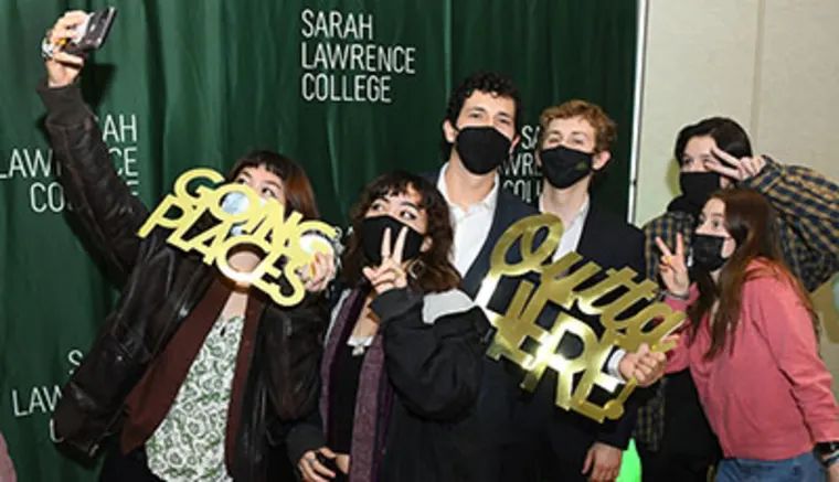 Group of people taking a selfie in front of a green Sarah Lawrence College backdrop, holding "Going Places" and "Outta Here" signs.