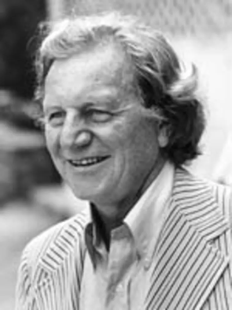 Smiling person with wavy hair wearing a striped blazer and collared shirt in an outdoor setting.