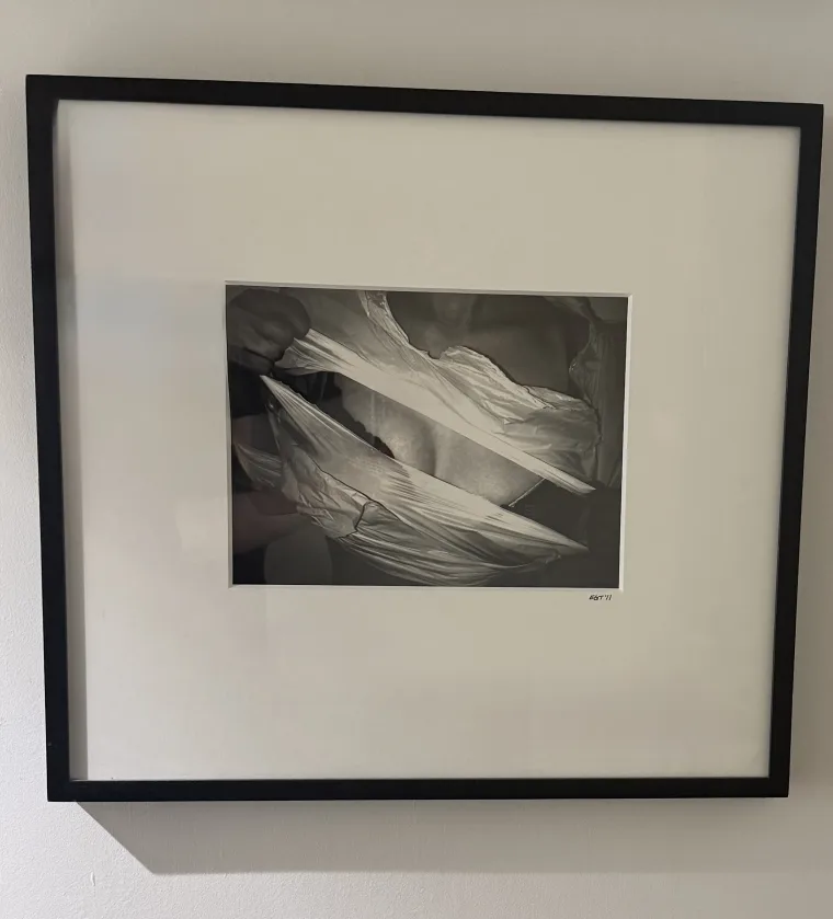 Framed black-and-white photograph of fabric being pulled apart, forming dynamic creases and shadows.
