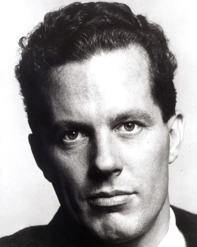 Close-up black and white photo of a person with curly hair, looking directly at the camera with a neutral expression.