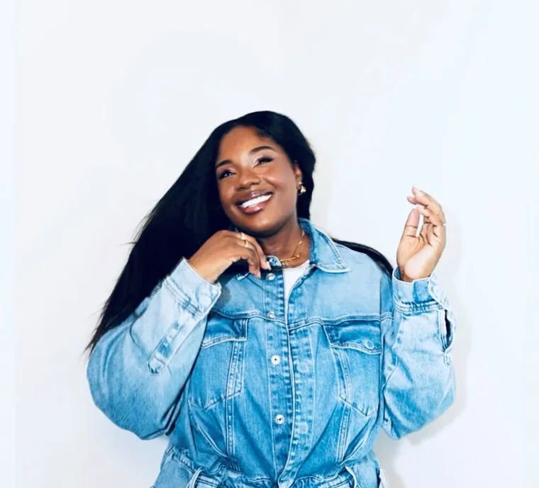 Person smiling and touching hair, wearing a denim shirt against a plain background.