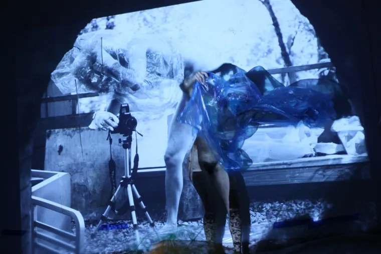 Abstract image showing a person wrapped in translucent material with a camera on a tripod, projected on a background of outdoor scenery.