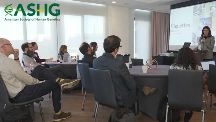 People seated in a conference room listen to a speaker presenting slides at an ASHG event.