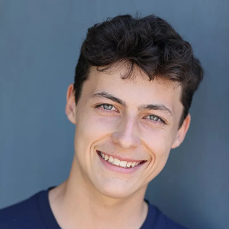 Person with short, dark curly hair smiling against a blue background.