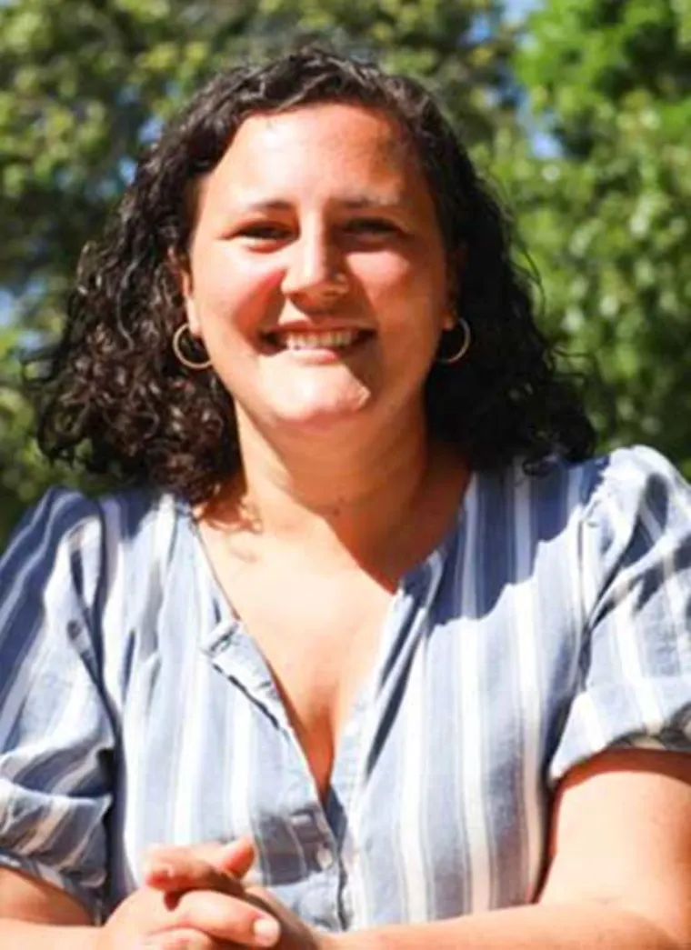 Person with curly hair smiling outdoors, wearing a striped shirt.