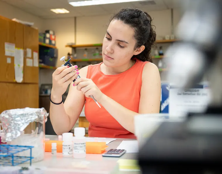 Person in an orange shirt working in a laboratory, using a pipette with various lab supplies on the table.