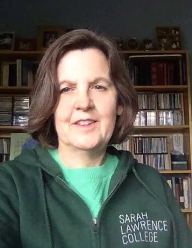 Person wearing a Sarah Lawrence College hoodie, smiling in front of a bookshelf filled with books and CDs.