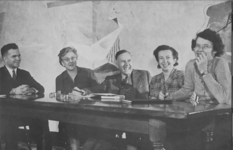 Five people sitting at a table, smiling and laughing, with a mural in the background.