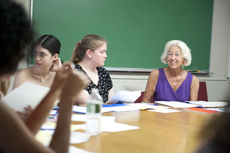 People sitting around a table with papers, discussing, in a room with a green chalkboard.