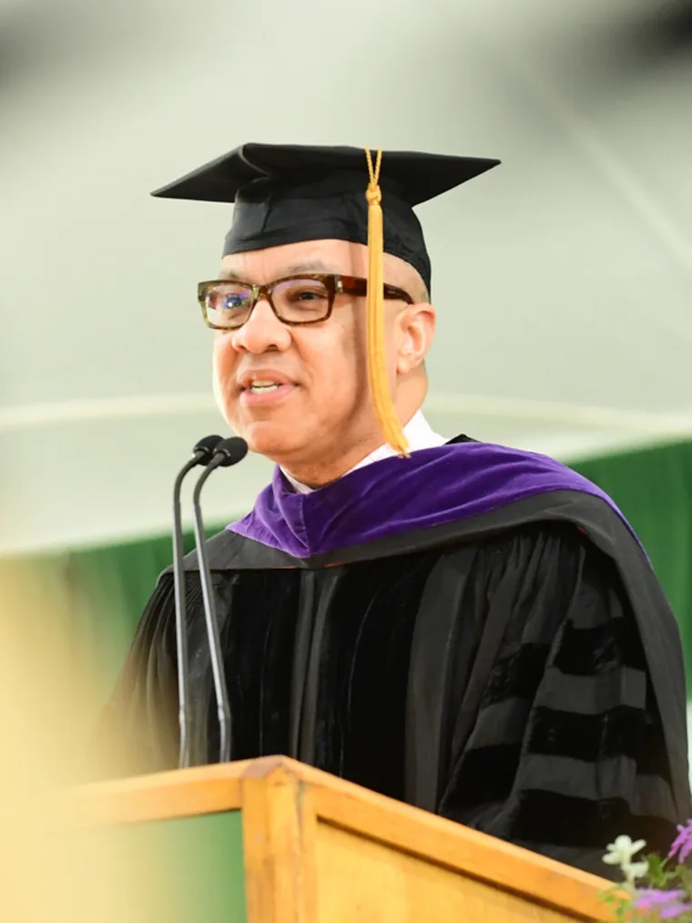 Person in graduation attire and cap speaking at a podium with a microphone.