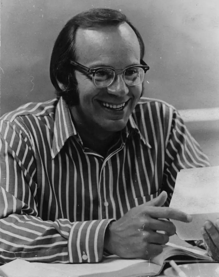Person smiling while pointing at a sheet of paper, wearing glasses and a striped shirt.