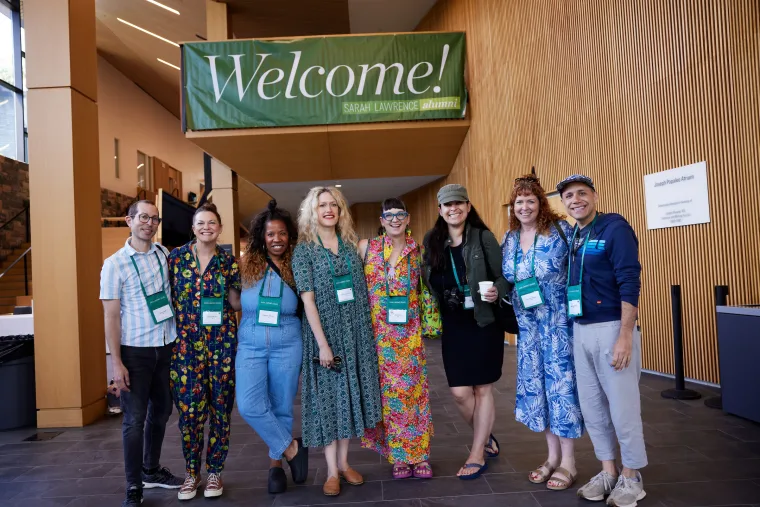 A group of people smiling under a "Welcome!" sign in a modern building, all wearing name tags.