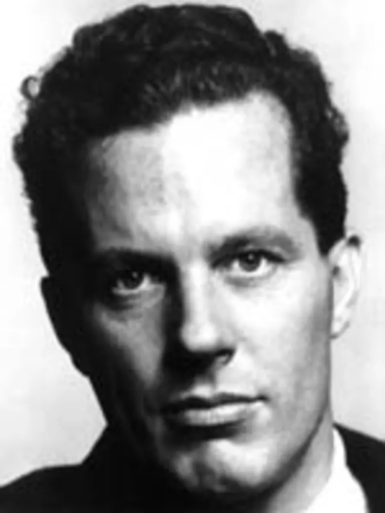 Black and white portrait of a person with short curly hair, wearing a suit, gazing directly at the camera with a serious expression.