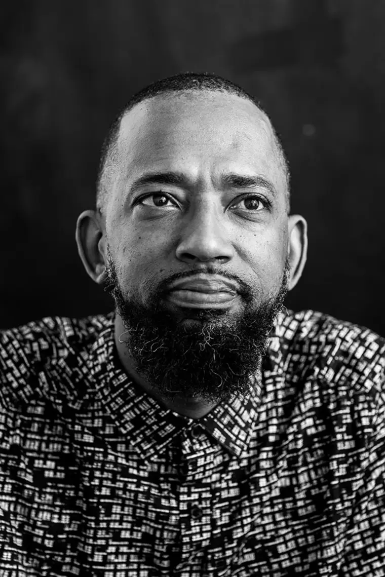 Person with a beard looks thoughtfully upward. Wears a patterned shirt. Black and white photo.