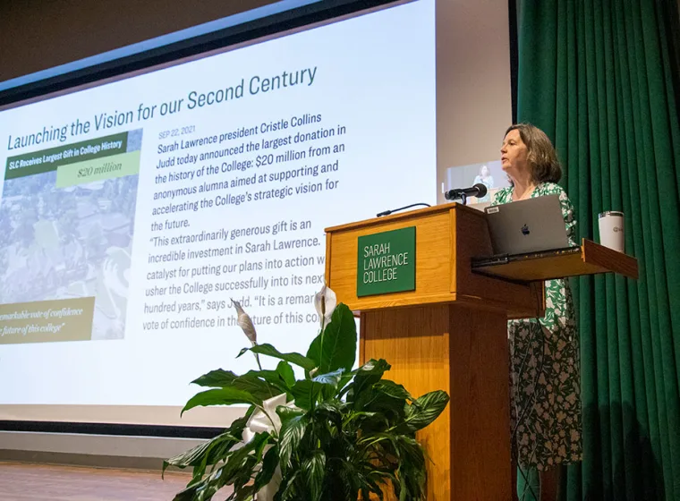 Person speaking at a podium with "Sarah Lawrence College" sign, next to projected slide about a $20 million donation for strategic vision.