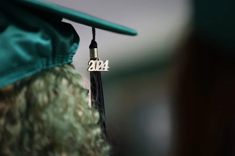 Close-up of a graduation cap with a tassel and "2024" charm, worn by someone with curly hair.