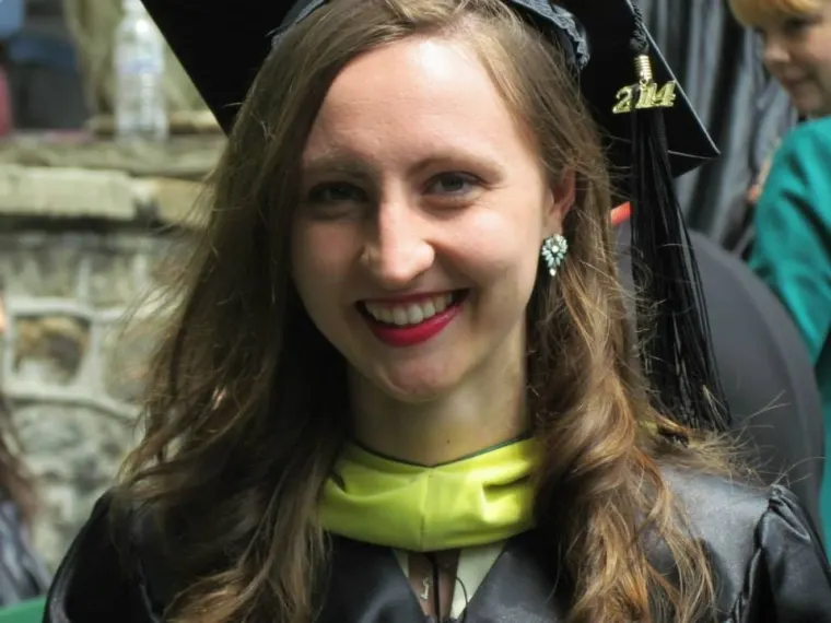 Person in graduation attire, wearing a cap with 2014 tassel, smiling.