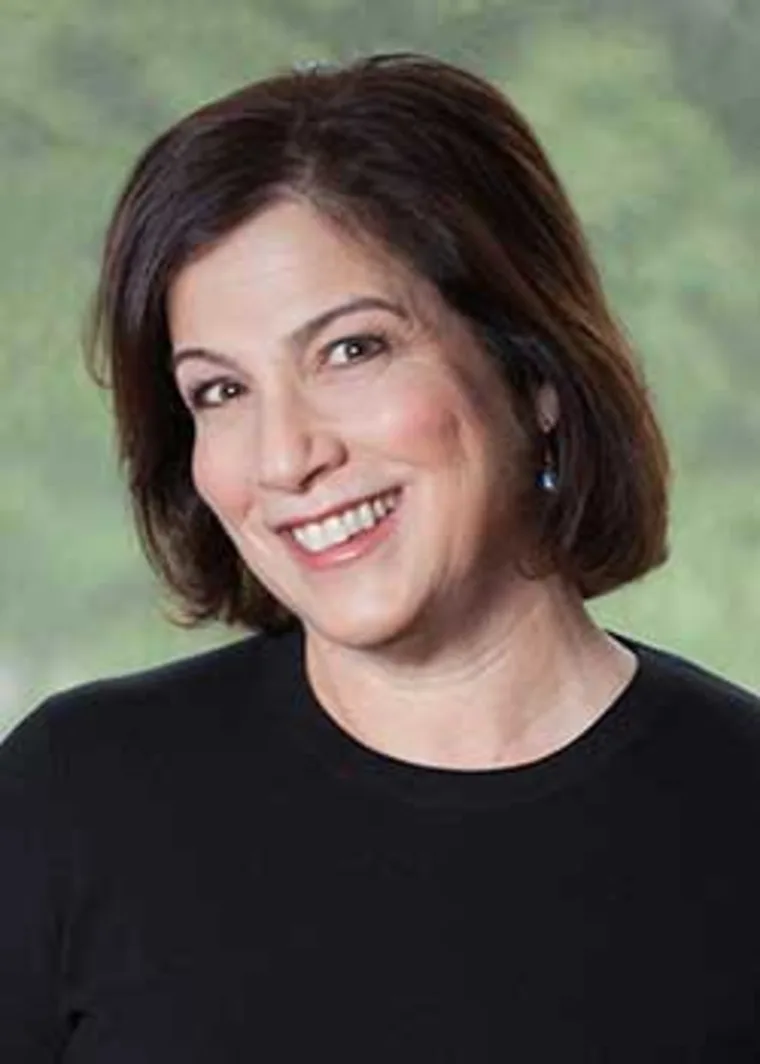 Smiling person with short dark hair in front of a blurred green background, wearing a black top.