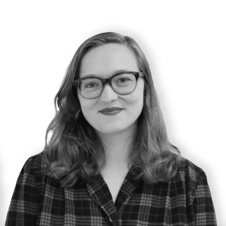 Person with glasses and long hair, wearing a plaid shirt, smiling against a plain white background.