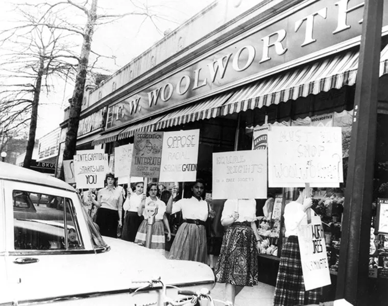 Protesters outside F.W. Woolworth store holding signs against segregation, advocating for integration and equal rights.