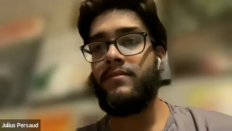 A person with glasses and a beard, wearing AirPods, looks towards the camera. A blurred background is visible. Text on screen shows: Julius Persaud.