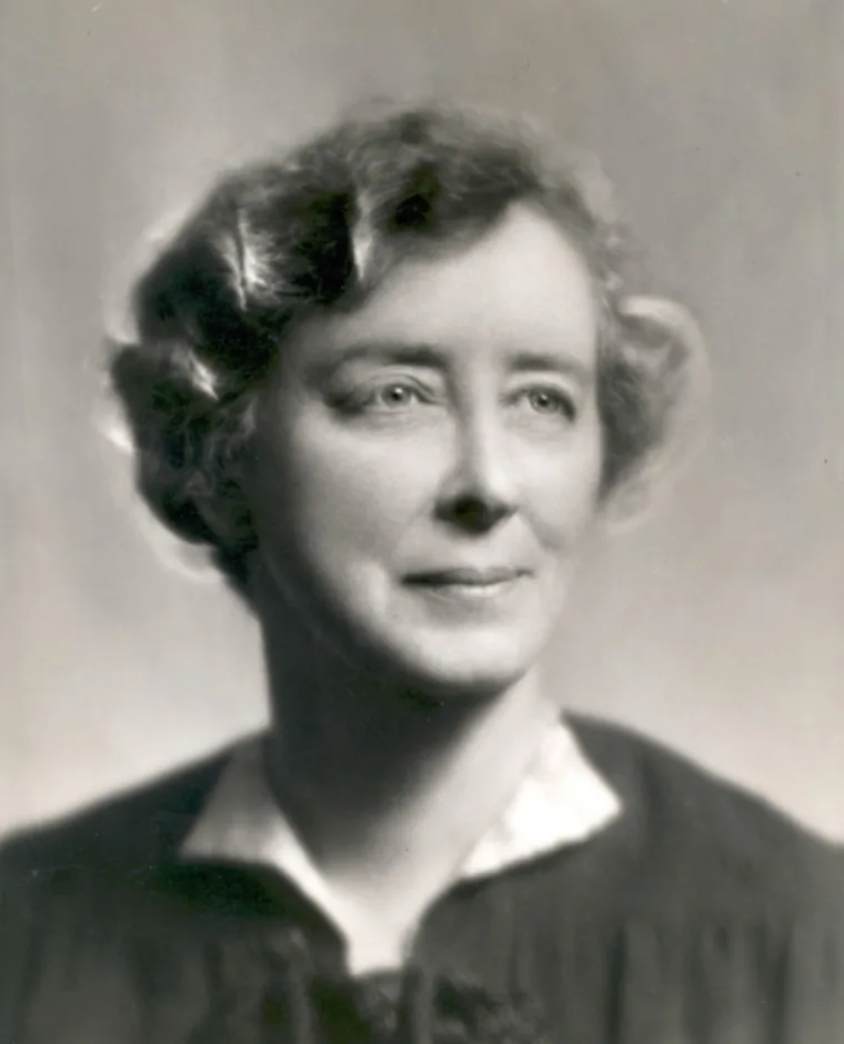 Black and white portrait of a person with short, wavy hair and a neutral expression, wearing a formal outfit.