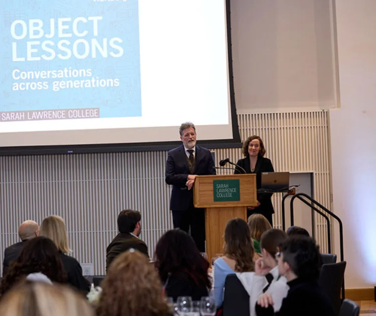 Two speakers stand at a podium labeled "Sarah Lawrence College" in front of a screen displaying "Object Lessons: Conversations across generations."