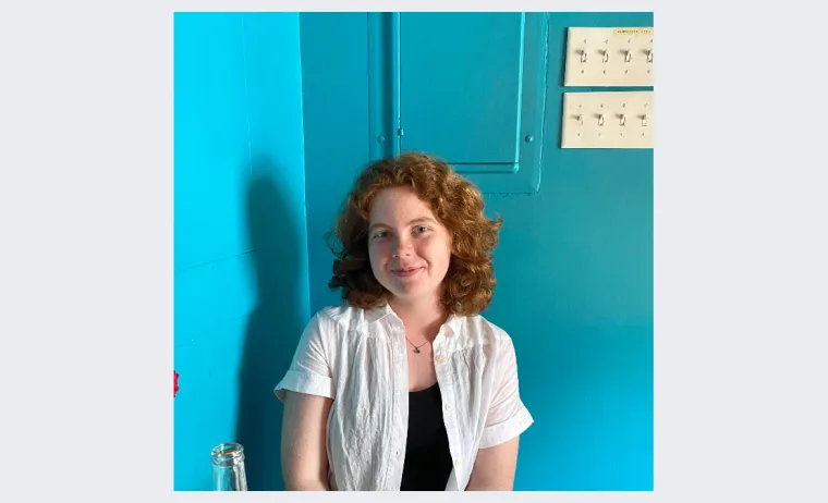 Person with curly hair wearing a white shirt sits against a bright blue wall.