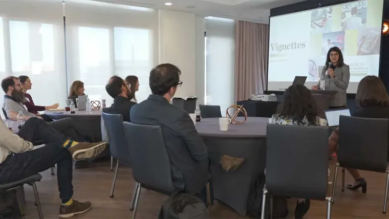 A person presents to a seated audience in a conference room. A screen displays "Vignettes" with various images.