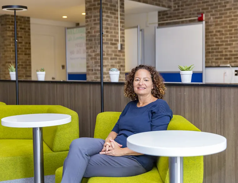 Person sitting on a lime green couch in a modern office, with round tables and small potted plants in the background.