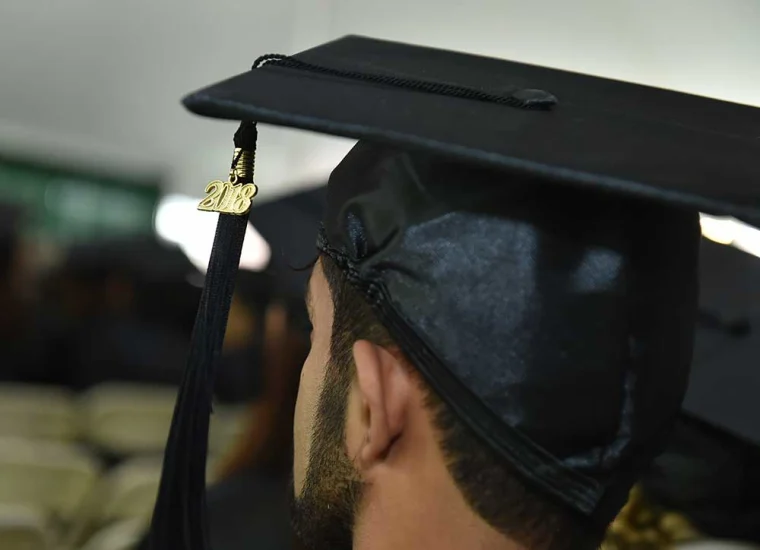 Close-up of a person wearing a graduation cap with a 2018 tassel, facing forward in a graduation ceremony setting.