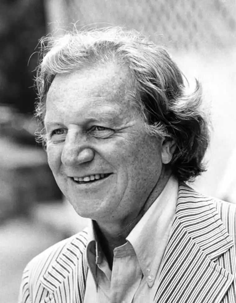 Smiling person with wavy hair in a striped blazer, viewed in black and white.