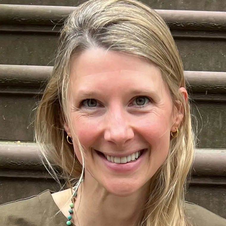 Person smiling while sitting on outdoor steps, with light hair and gold earrings.