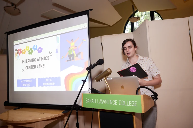 Person presenting at a podium with "Sarah Lawrence College" sign, next to a projection screen displaying "Interning at WJCS Center Lane."