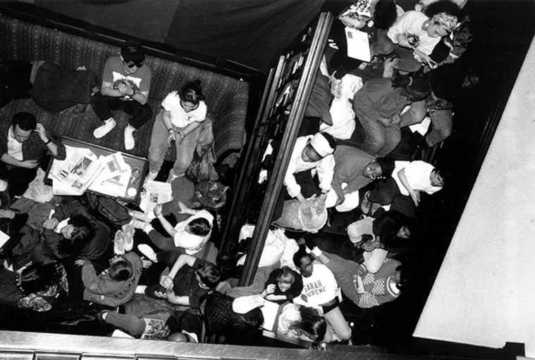 Crowded cafe with people sitting in booths and chairs, reading newspapers and chatting, viewed from above.