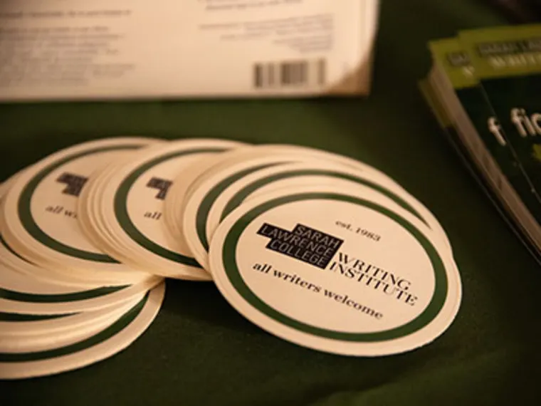 Circular coasters with "Sarah Lawrence College Writing Institute, all writers welcome" text, arranged on a table beside brochures.