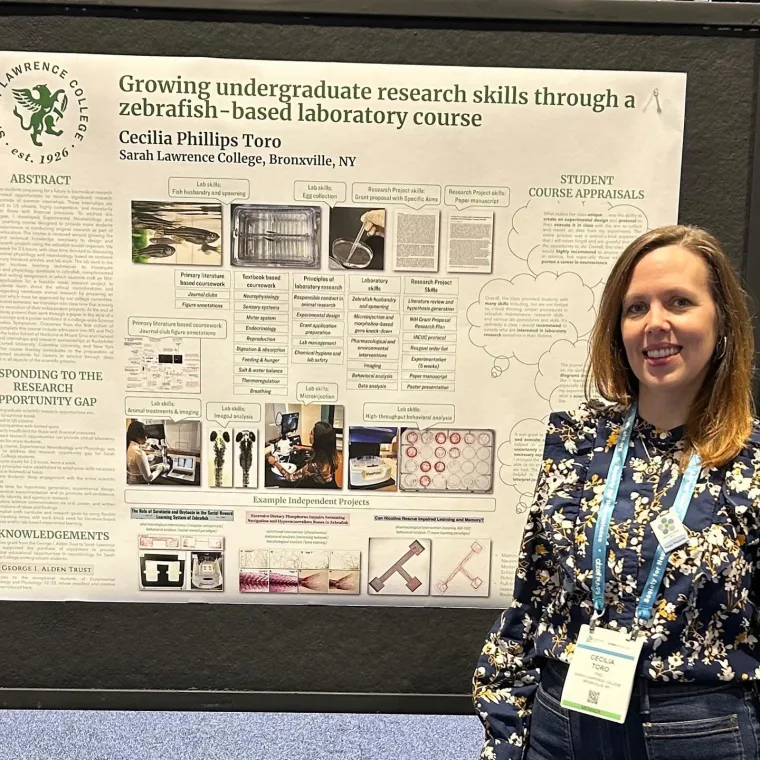 Person stands next to a research poster about zebrafish-based laboratory courses at a conference, wearing a floral shirt and conference badge.