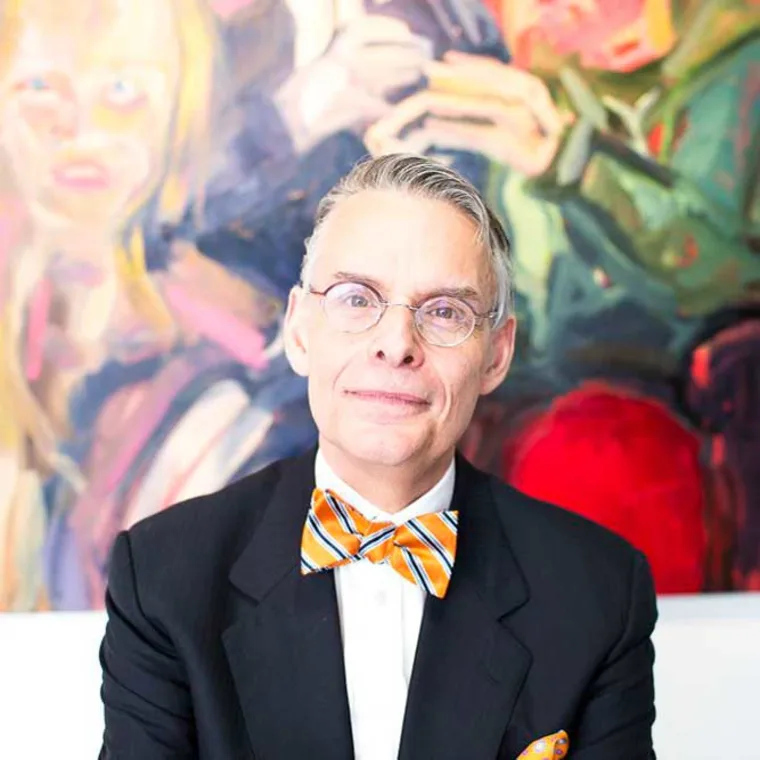 Person in suit and orange-striped bow tie stands in front of colorful abstract painting.