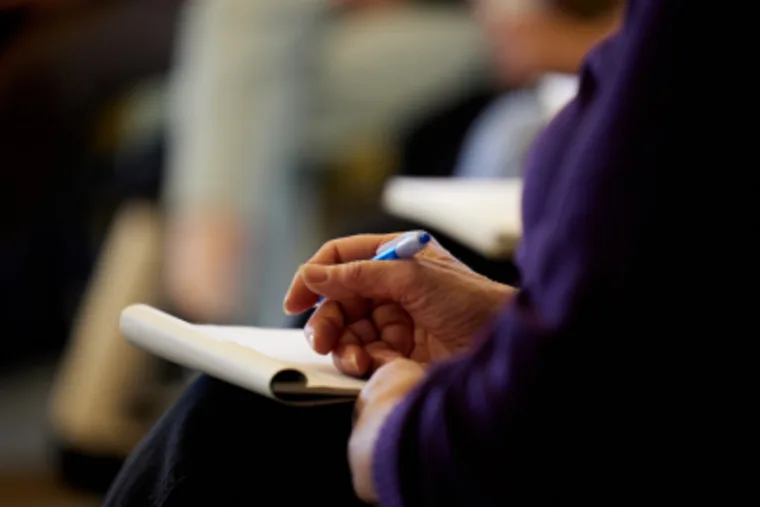 A person holds a blue pen, taking notes on a notepad, with a blurry background.