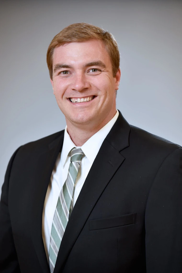 Person in a dark suit and striped tie smiling at the camera against a plain background.