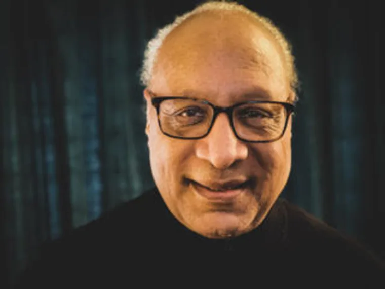 Person wearing glasses, smiling, against a dark background.