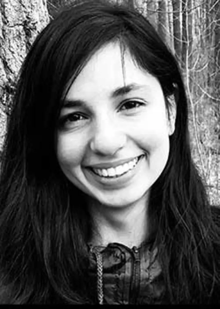 Smiling person with long hair in a black-and-white outdoor photo, standing near a tree.