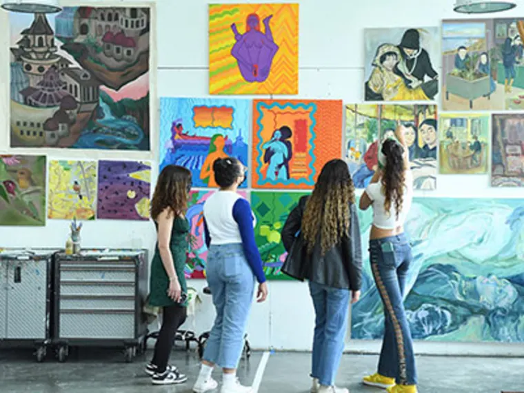 Four people stand in front of a wall displaying various colorful paintings in an art studio.