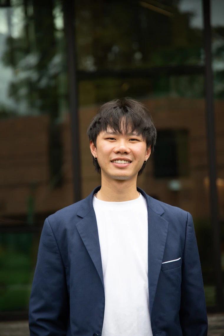 Person in a blue blazer and white shirt, smiling in front of a glass building facade.